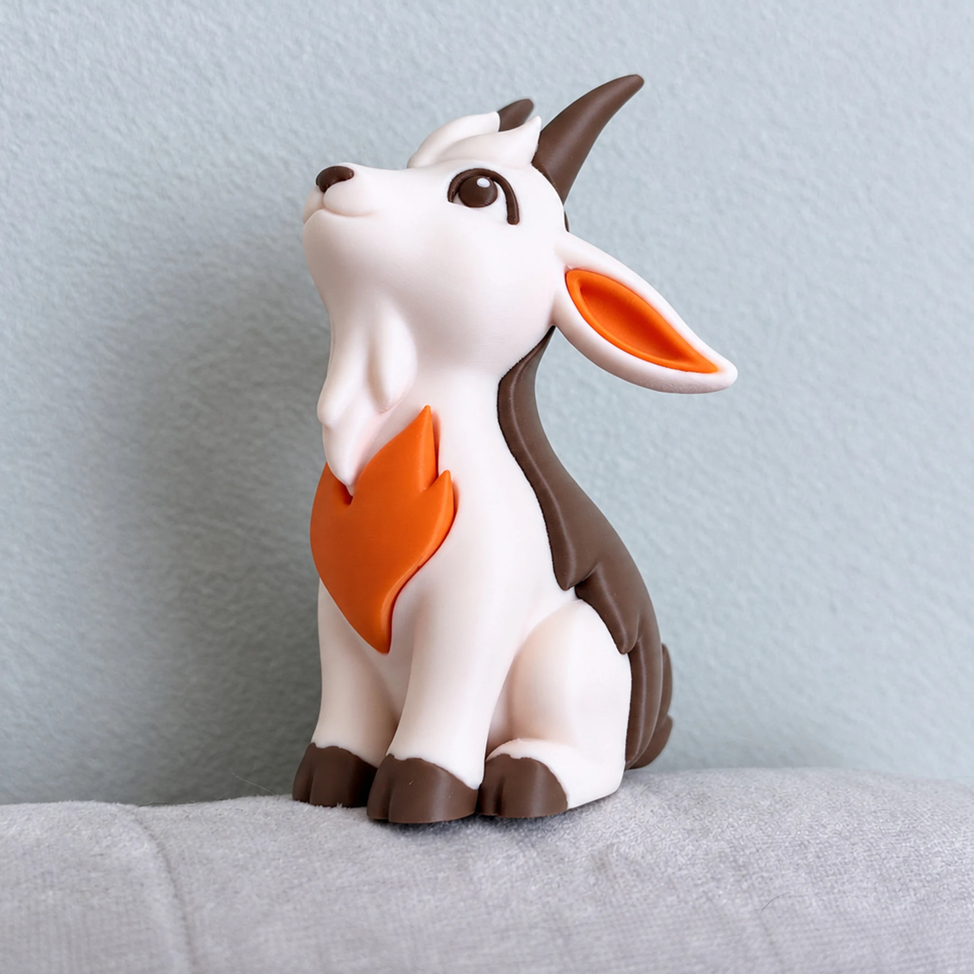 Brown and cream goat figurine without a base, with an orange flame motif on a light fabric background.