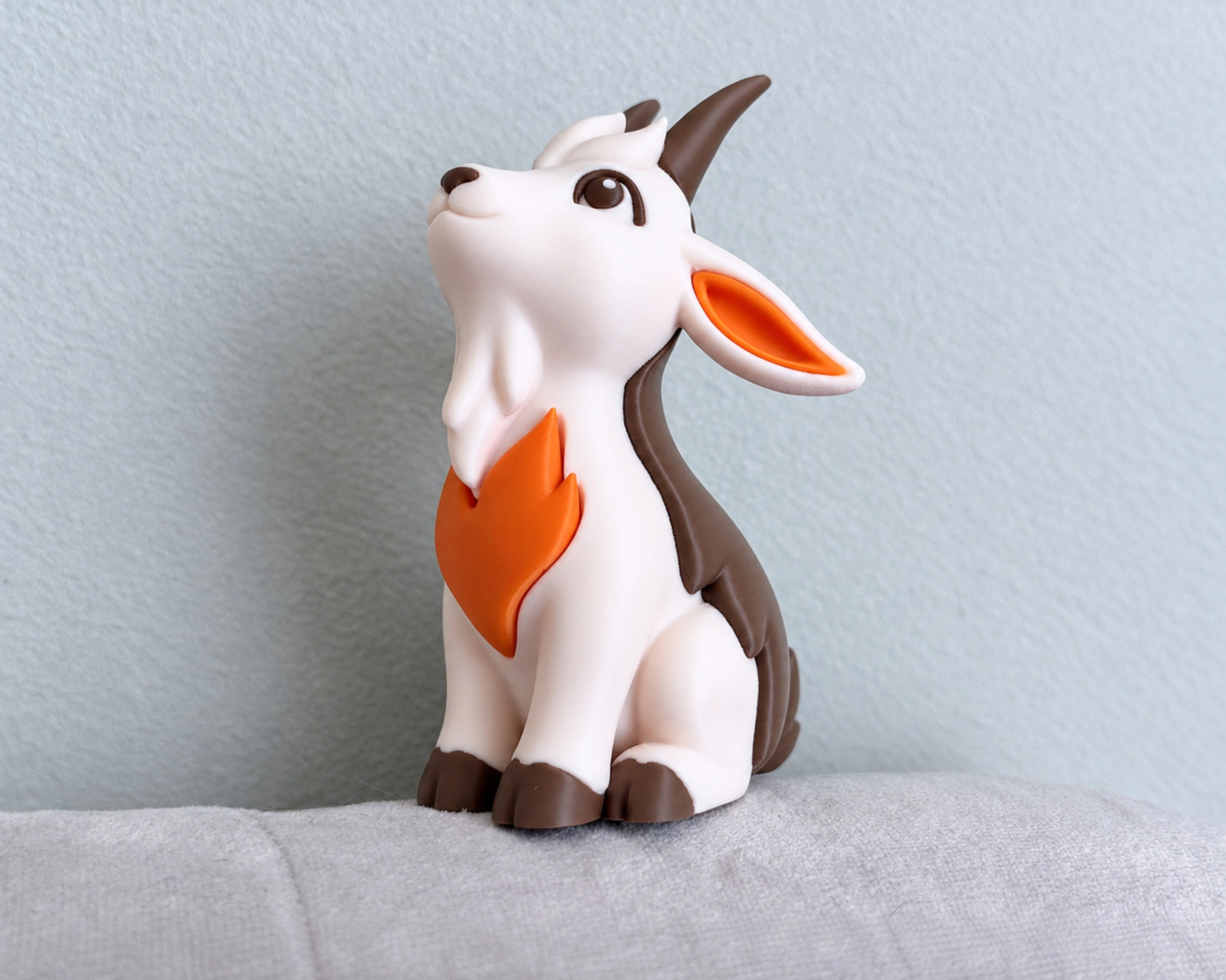 Brown and cream goat figurine without a base, with an orange flame motif on a light fabric background.